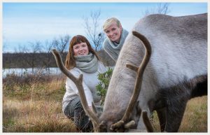 Gry og Ellen står bak en rein som gresser i naturlige omgivelser